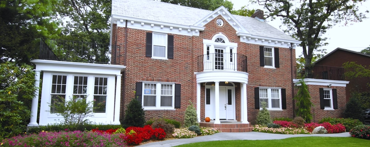 Red brick colonial house with white portico and flower beds